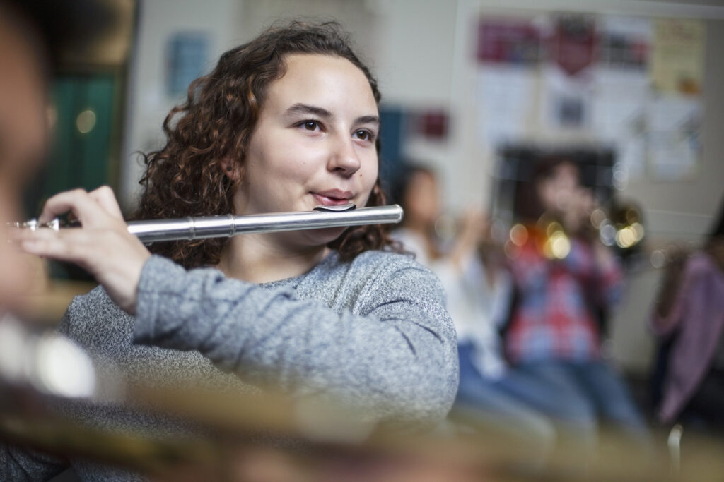 Confident female brunette student practicing flute in band orchestra class