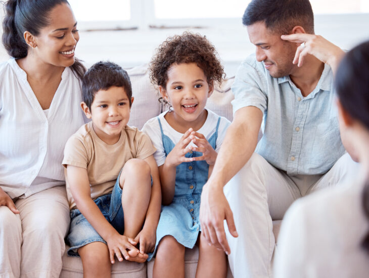 Parents, kids and counselling with psychology, smile and together on sofa, support and discussion. Young family, children and happy on couch with psychologist, listening and talking for mental health